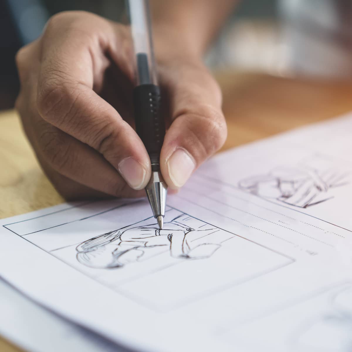 Main dessinant un croquis de personnage sur un storyboard avec un stylo sur du papier blanc.