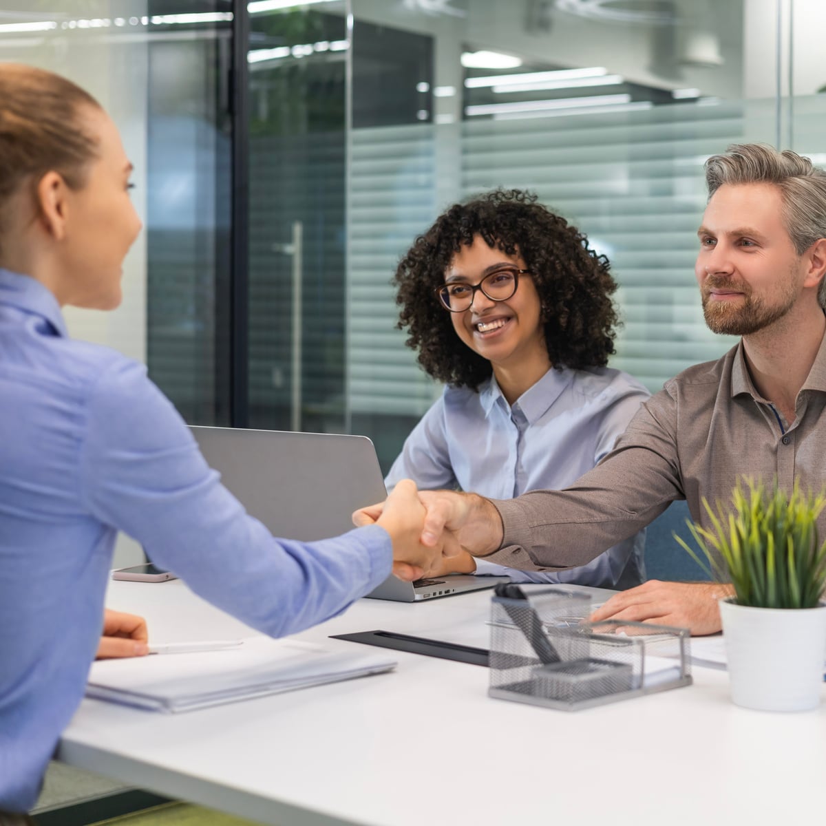 Poignée de main entre deux personnes lors d'une réunion de bureau. Une troisième personne regarde en souriant. Accord ou partenariat.